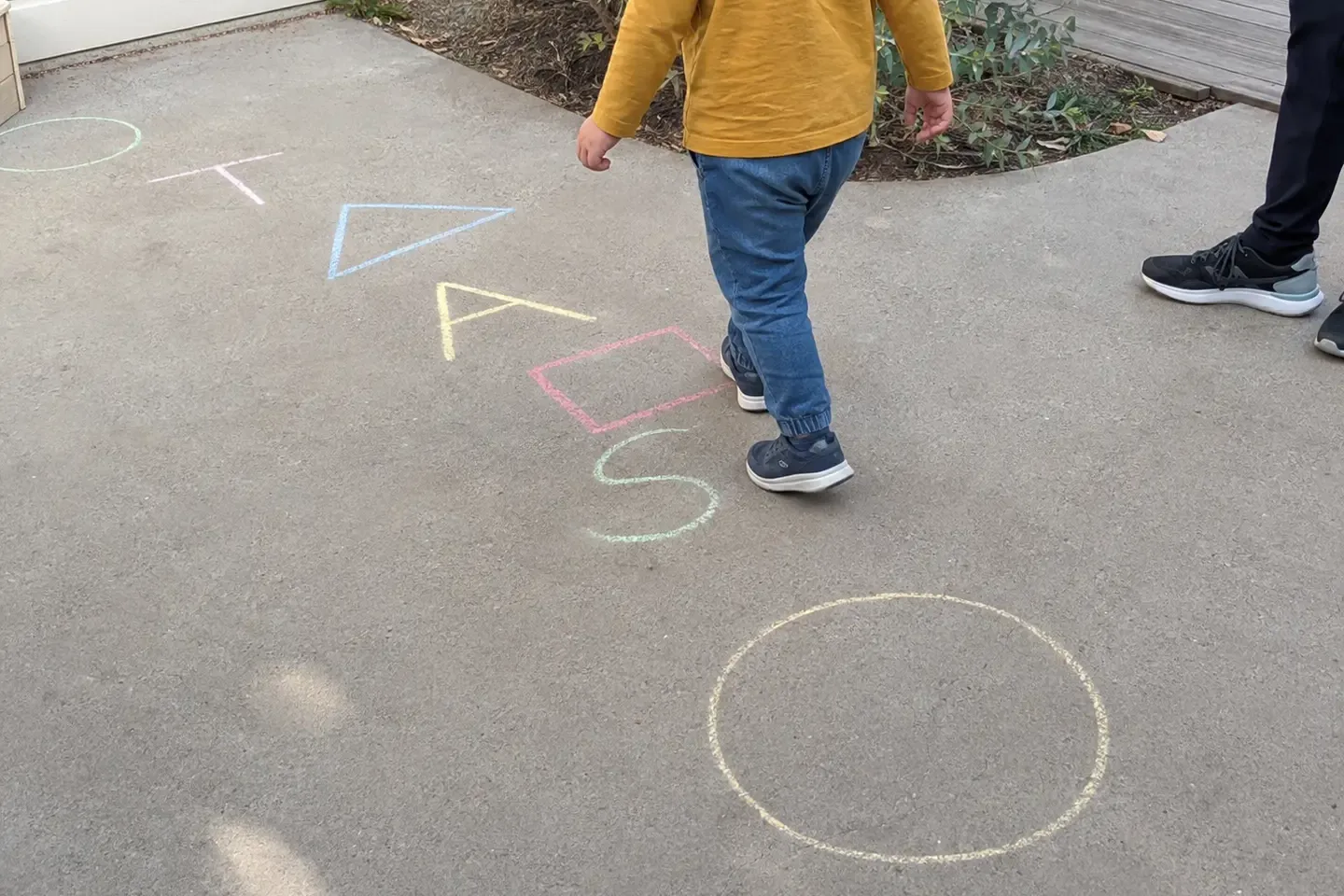 Preschool child following a colourful outdoor chalk path made from letters and shapes